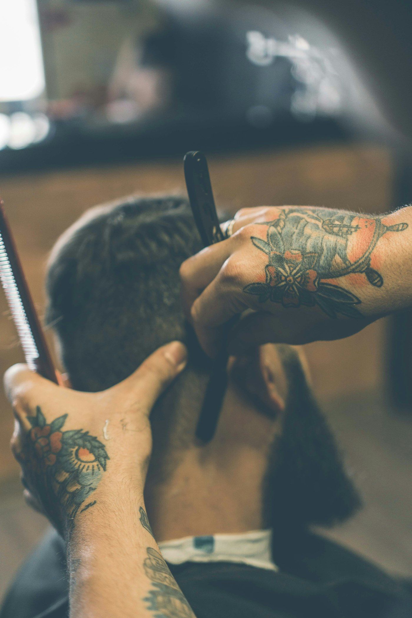 Stand-in Unsplash photo of a tattooed barber working a straight razor along a client's neckline